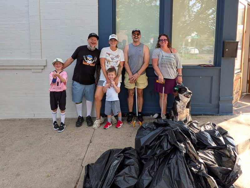 Four neighbors, two kids, and a dog standing with a pile of full trash bags after a cleanup